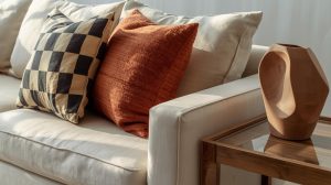 Zamansız tasarıma sahip bej keten koltuk üzerinde trend desenli yastıklar ve modern vazo detayı; ana mobilya ve aksesuar dengesi örneği.